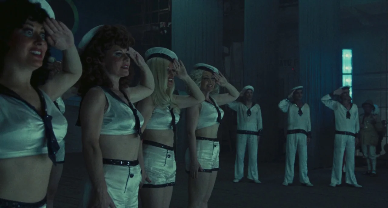 Roma (1972) movie still: medium — A dark, industrial-looking stage holds a group of performers dressed in matching sailor outfits. The performers…