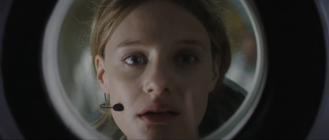 The Last Days On Mars (2013) movie still: closeup — A woman is framed within a circular portal against a dimly lit background. She stares forward…