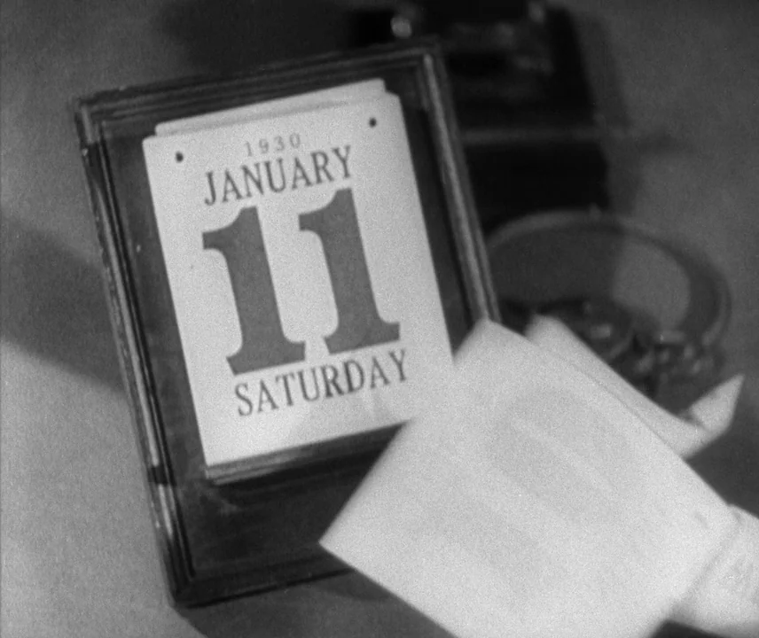 City Lights (1931) movie still: closeup — A close-up view shows a desktop calendar displaying Saturday, January 11, 1930. A hand is partially…