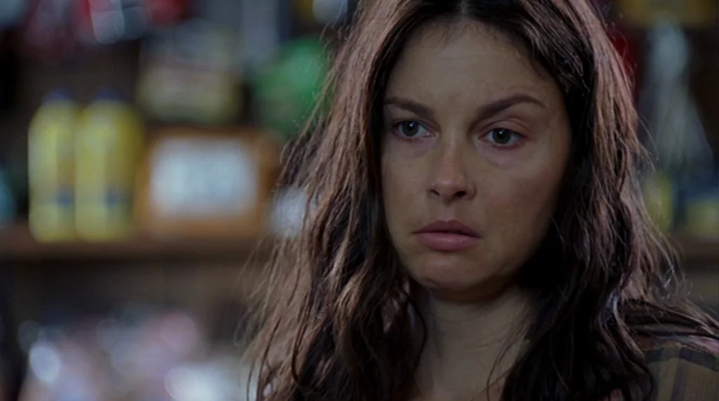 Bug movie still: closeup — A close-up shot focuses on a woman in a retail environment with blurred products. She looks directly toward a point just…