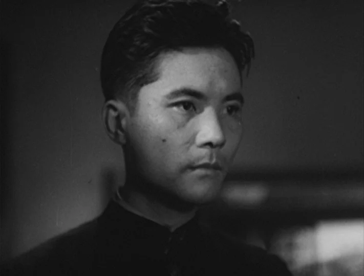 No Regrets for Our Youth (1946) movie still: closeup — A dimly lit indoor space with heavy shadows obscuring the background details. A young man…