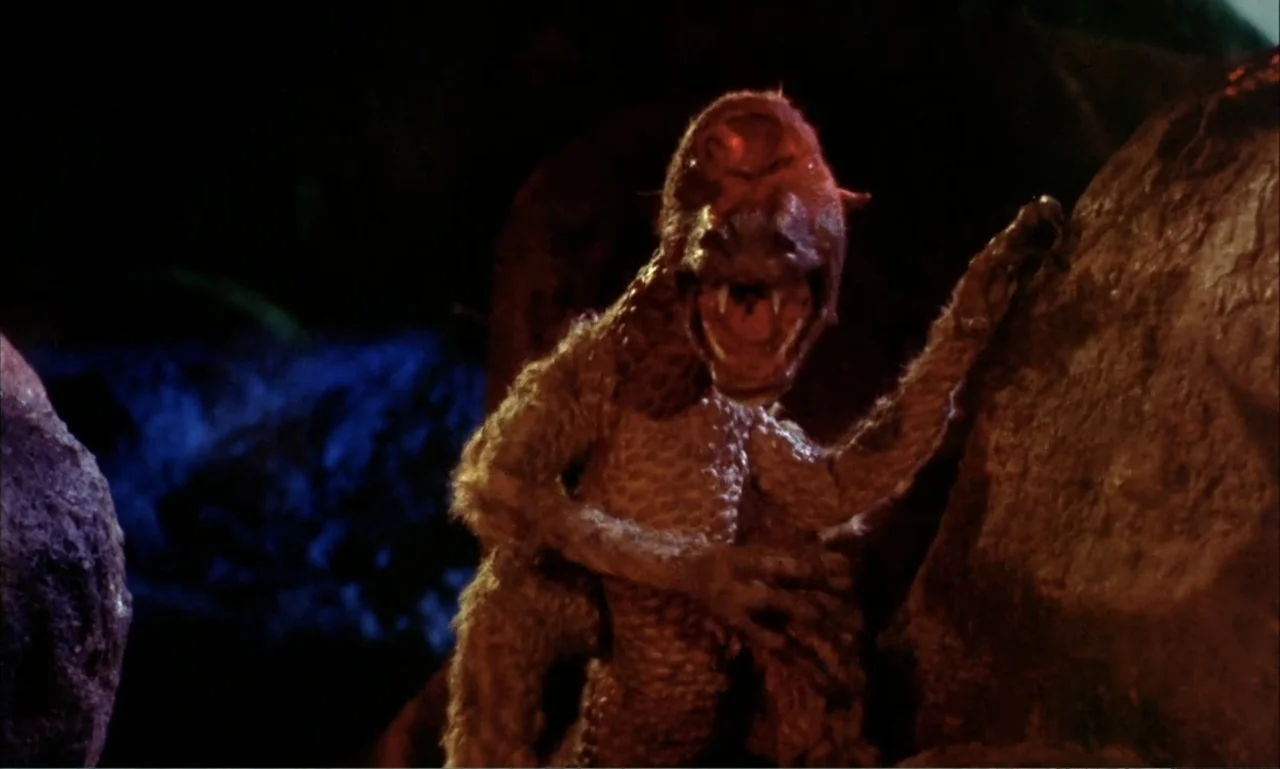 Journey to the Seventh Planet (1962) movie still: medium — A dark, rocky area with a textured creature emerging from behind a large stone. The…