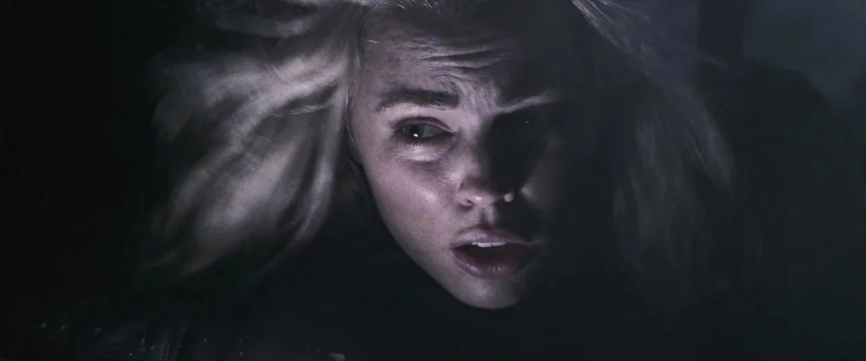 30 Days of Night (2007) movie still: closeup — A person with pale blonde hair is seen against a pitch-black background. Their face is illuminated by…