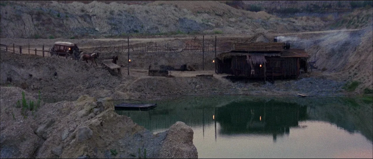The Grand Duel (1972) movie still: establishing — A rural mining camp sits in a barren, excavated quarry next to a stagnant pond. A small weathered…