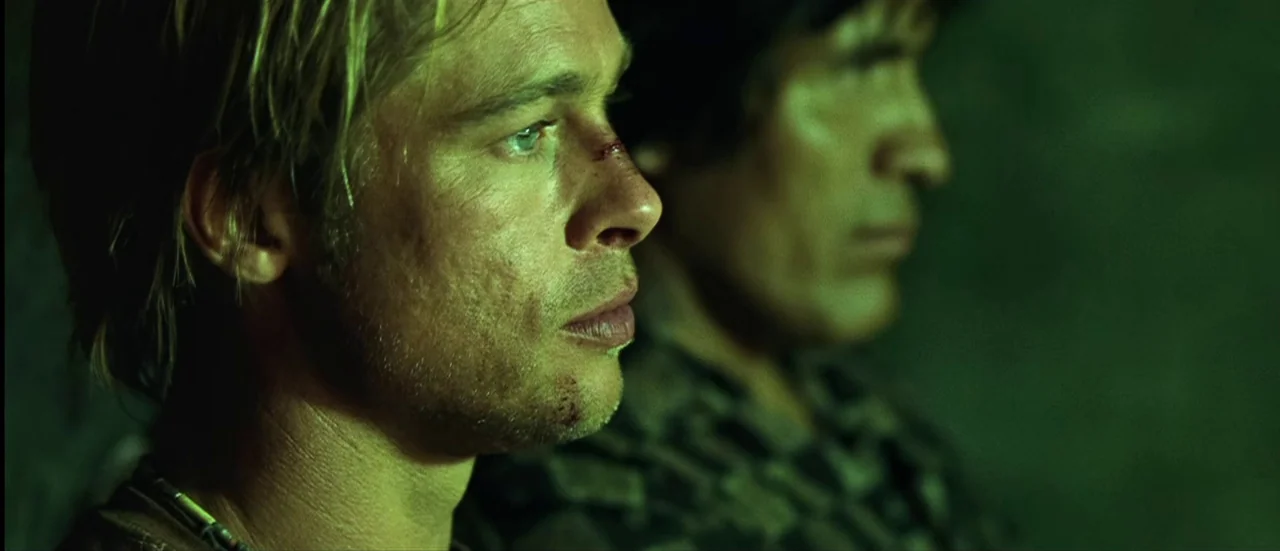 The Mexican (2001) movie still: closeup — Two men sit in a dimly lit, green-tinted environment. The man in the foreground has small facial abrasions…