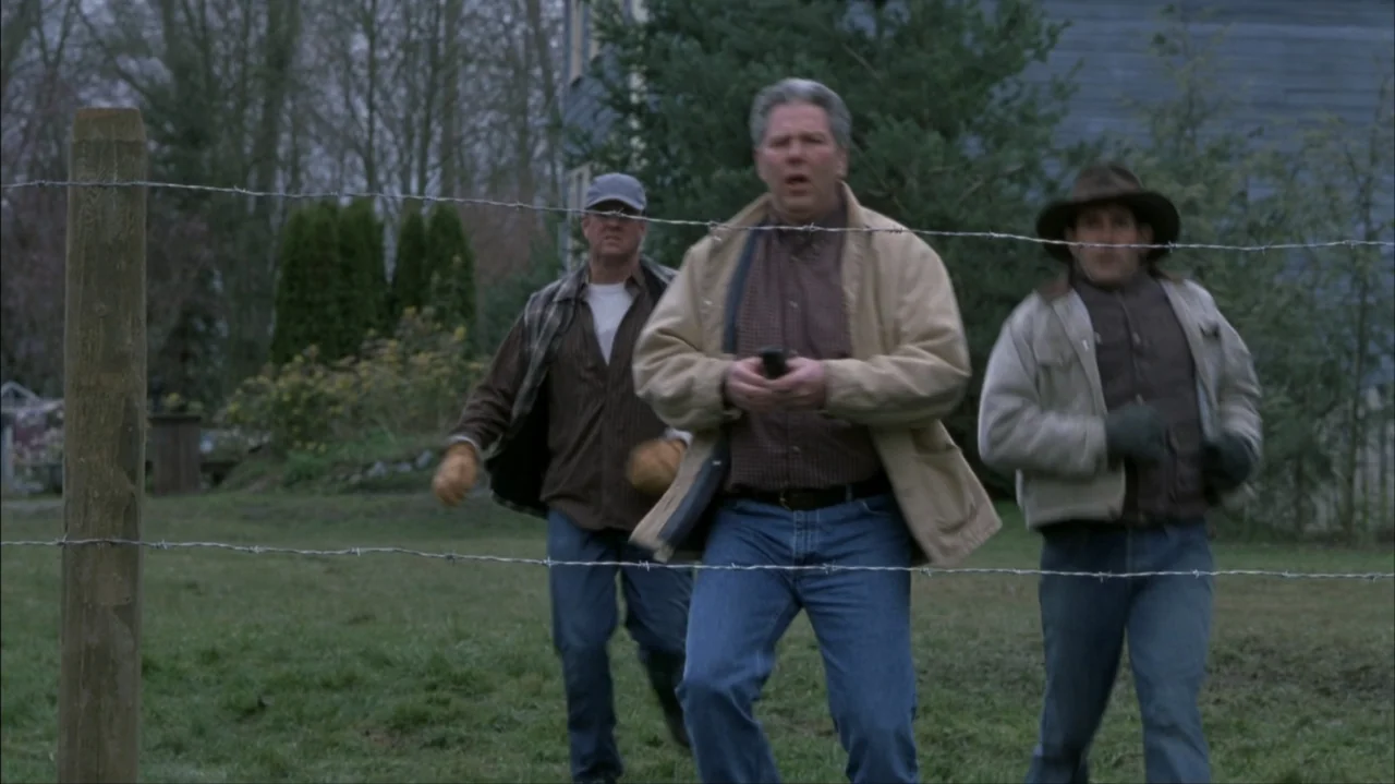 Final Destination 2 (2003) movie still: fullbody — An open grassy field contains a wire fence stretching across the foreground. Three men walk…
