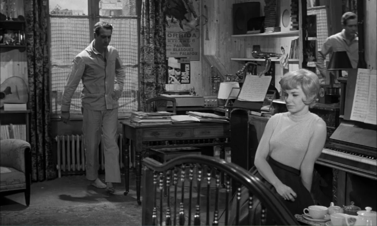 Paris Blues (1961) movie still: medium — A cluttered apartment room features a writing desk, a piano, and large window curtains. A man in pajamas…