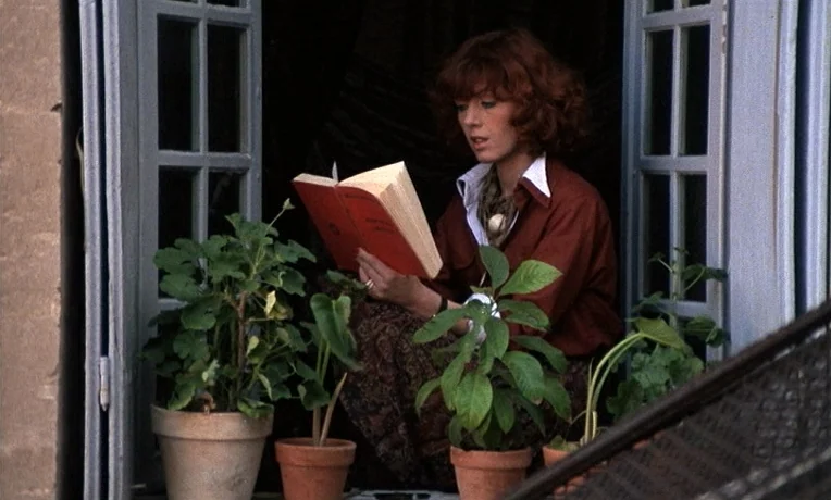 The Man Who Loved Women (1977) movie still: medium — A woman sits at an open window surrounded by several potted green plants. She focuses on…