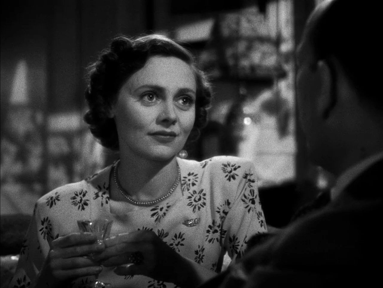 In Which We Serve (1942) movie still: medium — A dimly lit indoor space with blurred architectural elements and restaurant booth seating. A woman in…
