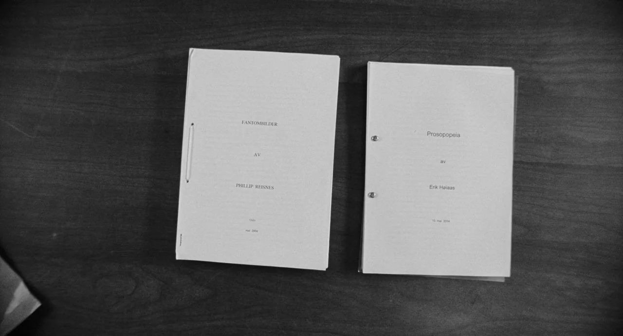 Reprise (2006) movie still: closeup — A wooden desktop surface holds two separate paper manuscripts side by side. The documents are bound with…