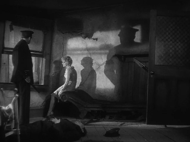 The Docks of New York (1928) movie still: wide — A dark apartment room features cracked walls and a person lying on the floor. A uniformed man…