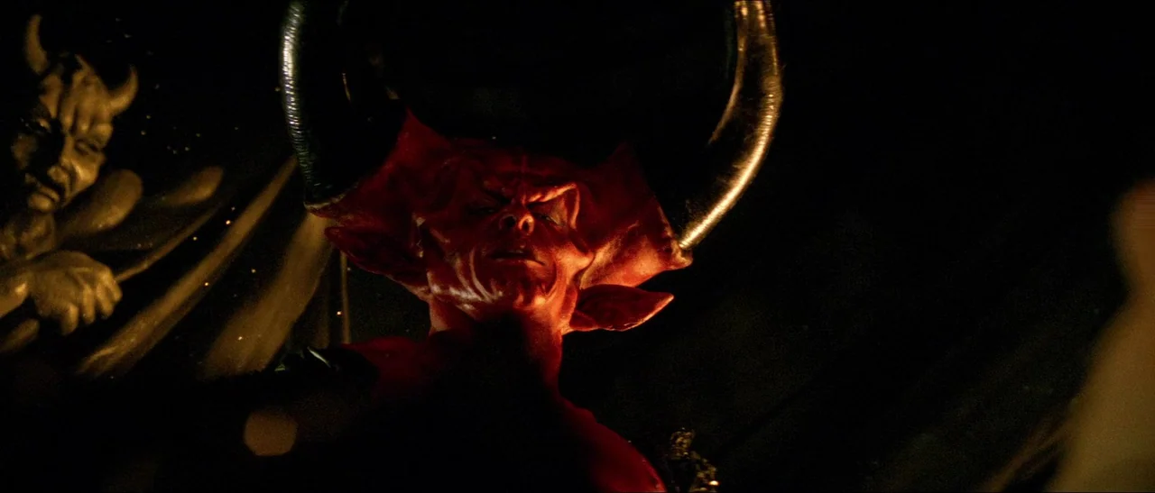 Legend (1985) movie still: medium — A dark, cavernous space features a red-skinned creature with massive, curved black horns. The figure looms…