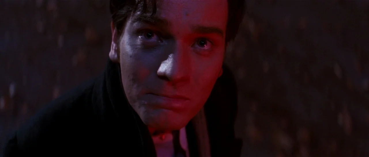 Moulin Rouge! (2001) movie still: closeup — A man stands in a dark space illuminated by a harsh red light source. He looks upward with a neutral…