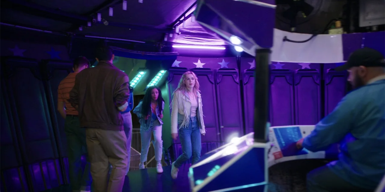 Totally Killer (2023) movie still: medium — A dimly lit room features walls decorated with star patterns and purple neon lighting. Several young…