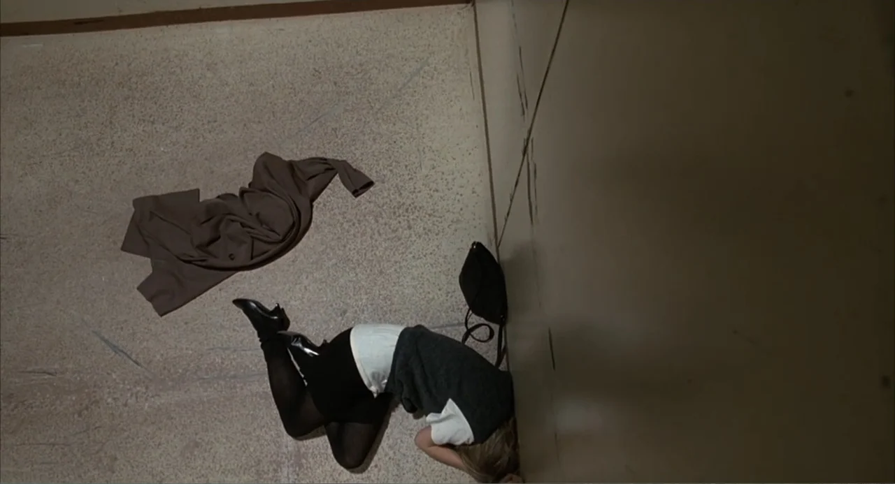 I, Madman (1989) movie still: wide — A utilitarian elevator interior features light beige walls and a speckled floor. A person lies curled in the…