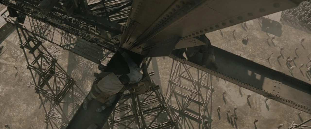 Eiffel (2021) movie still: wide — A high-altitude steel construction frame overlooks a vast dusty lot with distant figures. Two men hold onto the…