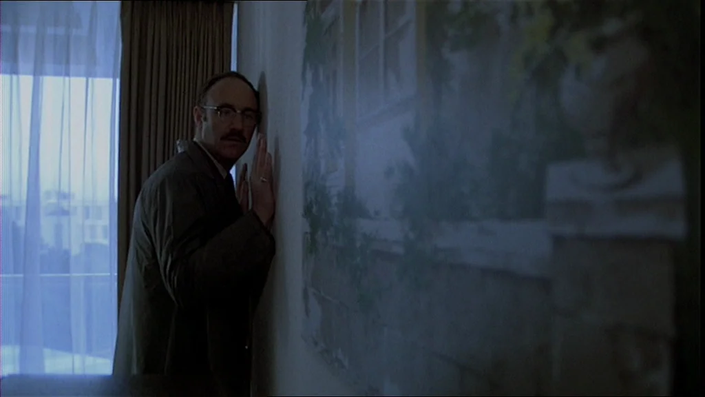 The Conversation (1974) movie still: medium — A dark hotel room interior features a large mural on the wall. A middle-aged man stands against the…