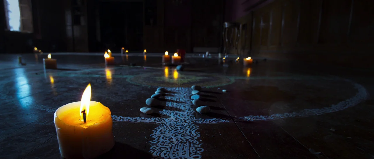 A Dark Song (2016) movie still: wide — A dark wooden floor is marked with intricate white ritual patterns and small stones. Multiple wax candles are…