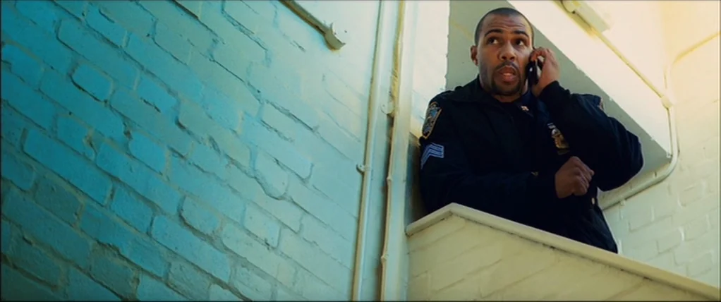 Kick Ass (2010) movie still: medium — A stairwell with pale painted brick walls and a metal railing. A man in a police uniform stands against the…