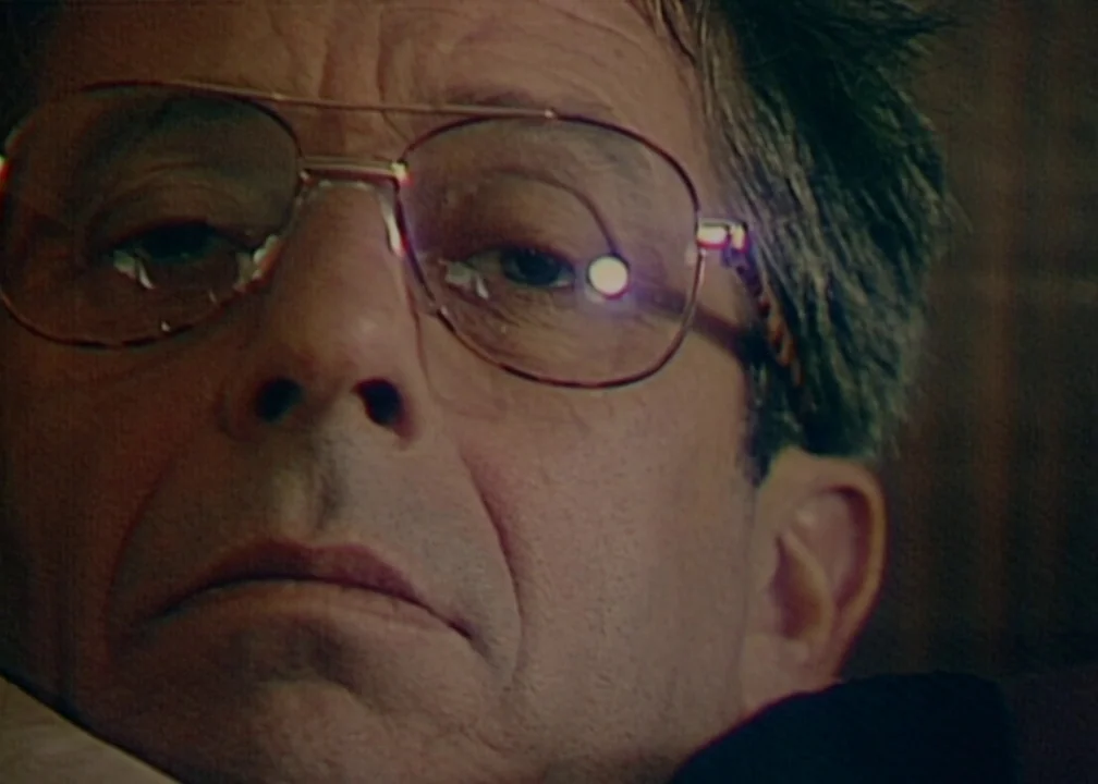 No (2012) movie still: closeup — A close view of an older man's face set against a dark background. He wears large wire-rimmed glasses while looking…