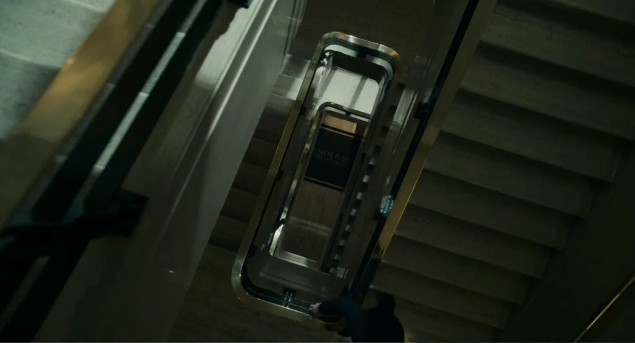 Back to Black (2024) movie still: establishing — An interior stone staircase viewed from directly above in a multi-story building. The central…
