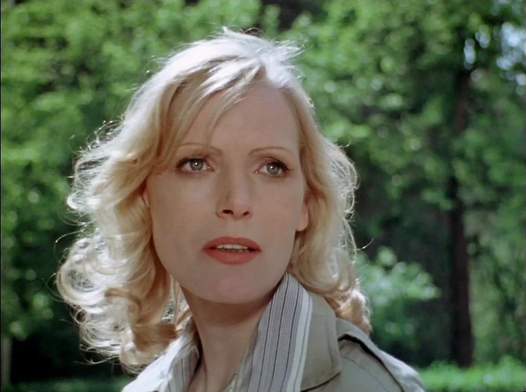 Fear Of Fear (1975) movie still: closeup — A woman stands outdoors with out-of-focus green trees in the background. She looks toward the side of the…