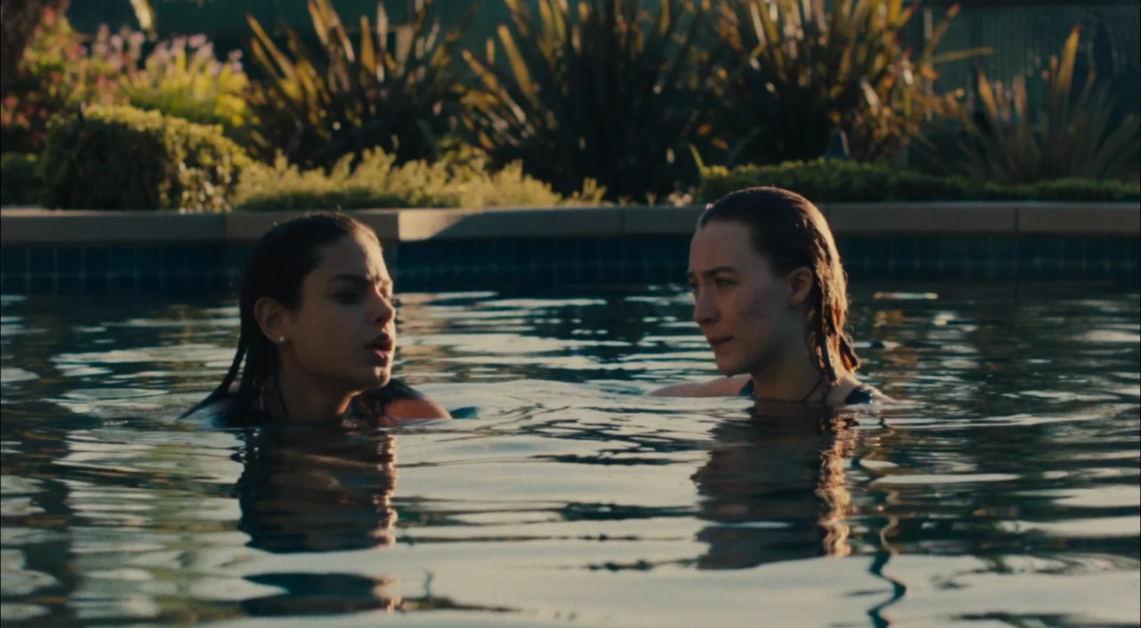 Lady Bird (2017) movie still: medium — Two women are partially submerged in the water of a backyard residential swimming pool. They face one another…