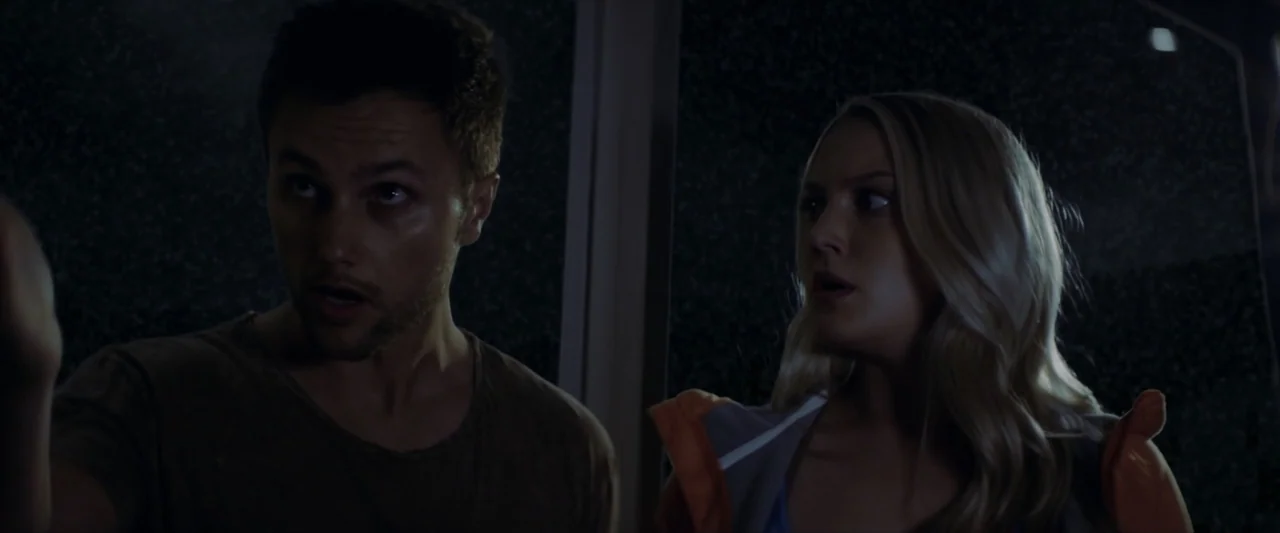 Tell Me How I Die (2016) movie still: medium — Two individuals stand in a dark, indistinct interior environment at night. They look toward the side…