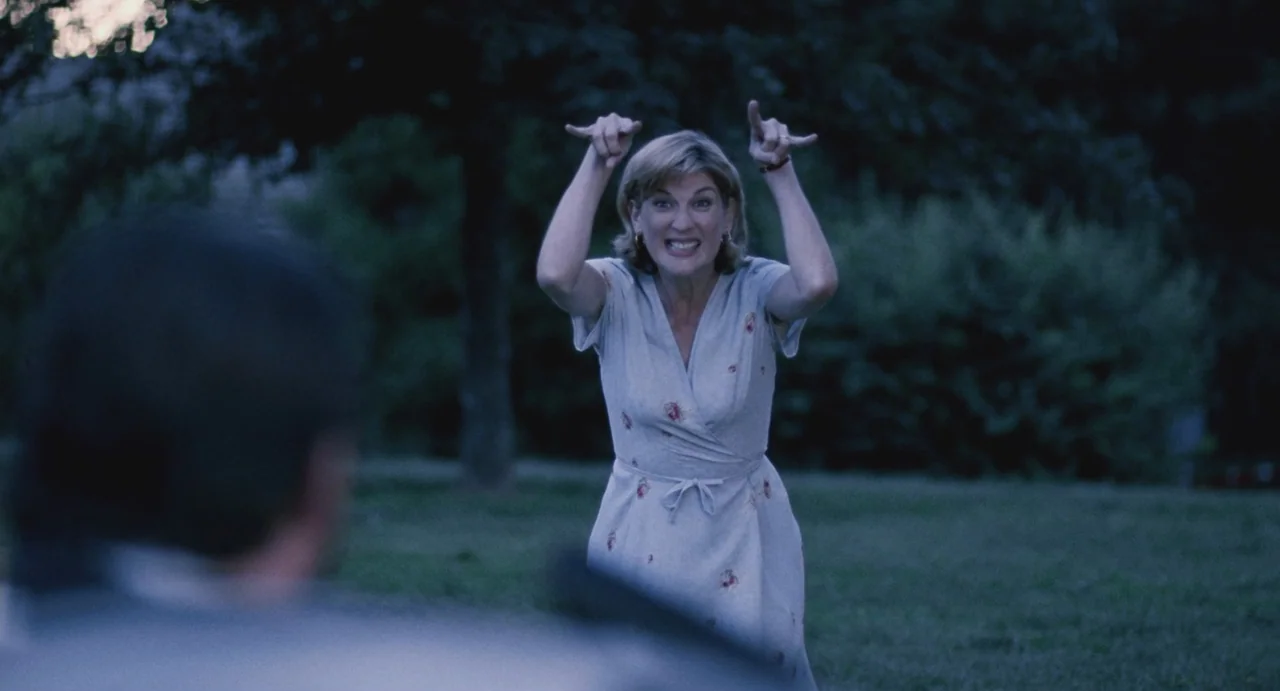 Ma Vie En Rose (1997) movie still: medium — A park lawn at dusk features a woman facing a second, partially obscured person. The woman raises both…