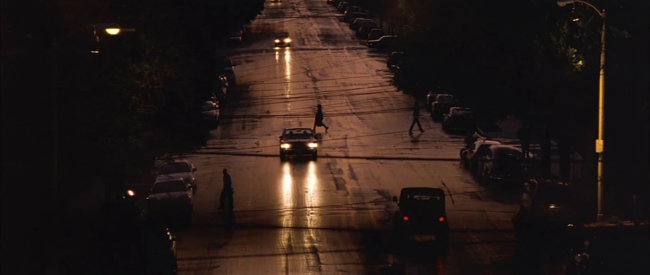 Training Day (2001) movie still: wide — A dark, wet city street is illuminated by moving vehicle headlights and overhead streetlights. Several…