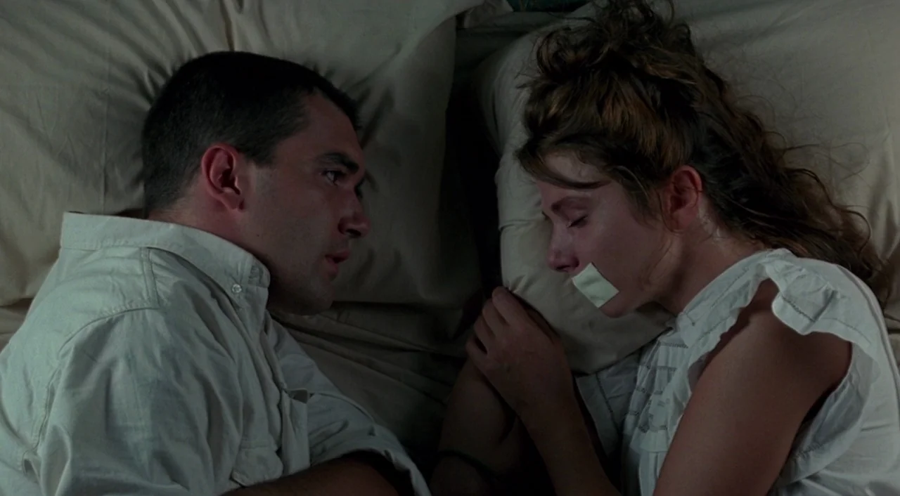 Tie Me Up! Tie Me Down! (1989) movie still: medium — A man and a woman lie in bed on light beige linens. The woman has a piece of white adhesive…