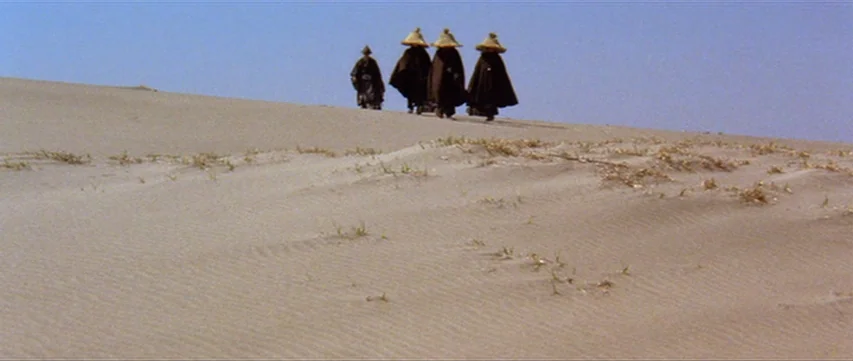 Lone Wolf: Baby Cart at the River Styx (1972) movie still: wide — A vast expanse of rolling sand dunes stretches under a clear, pale blue sky. Four…