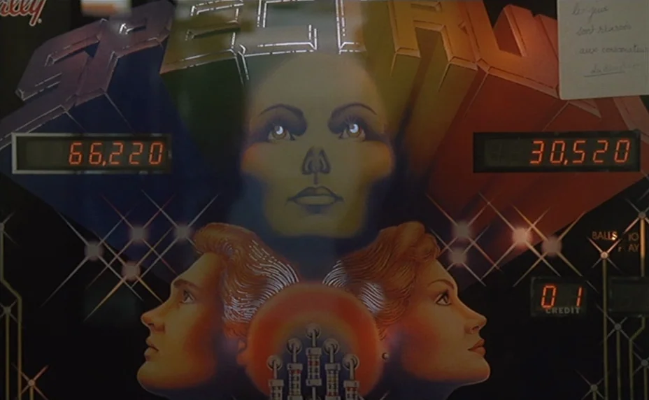 Kung Fu Master! (1988) movie still: closeup — A close-up of a pinball machine backglass features stylized faces and digital score displays. Two…