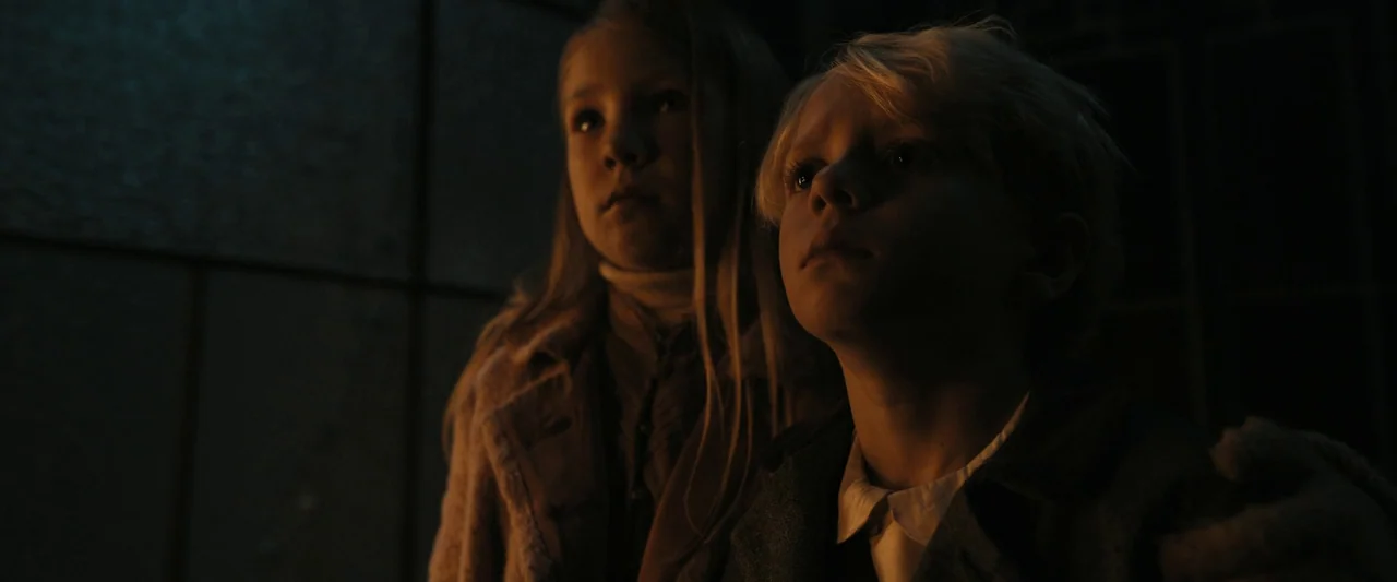 The Hunger Games: The Ballad of Songbirds & Snakes (2023) movie still: medium — Two children stand in a dark, dimly lit space with high contrast…