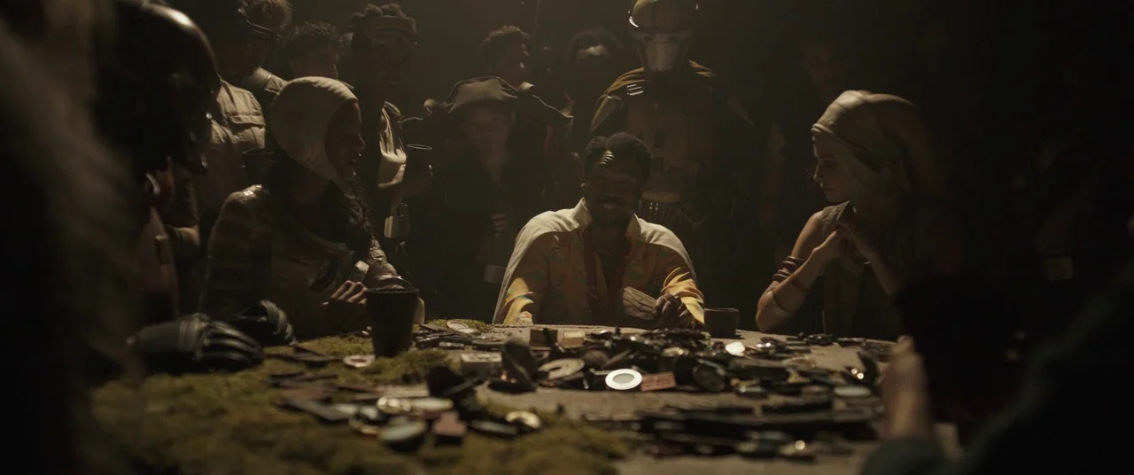 Solo: A Star Wars Story (2018) movie still: medium — A dimly lit room features a large circular table covered in various metallic objects. A man in…