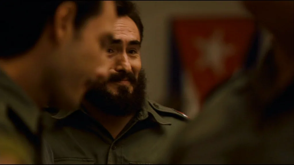 Che Part 2 (Guerrilla) (2008) movie still: medium — A dimly lit room contains multiple individuals dressed in 1950s era military uniforms. A bearded…