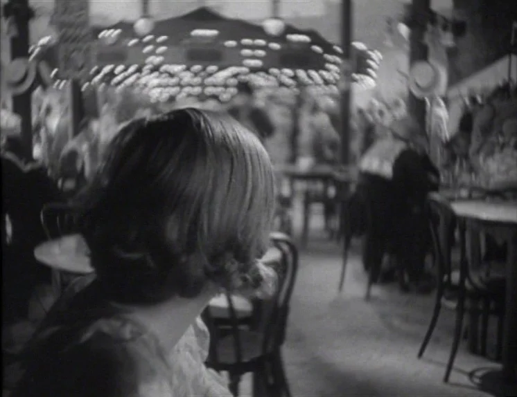 Anna Christie (1930) movie still: medium — A dimly lit indoor space with circular tables and chairs in the foreground. A woman sits in the…