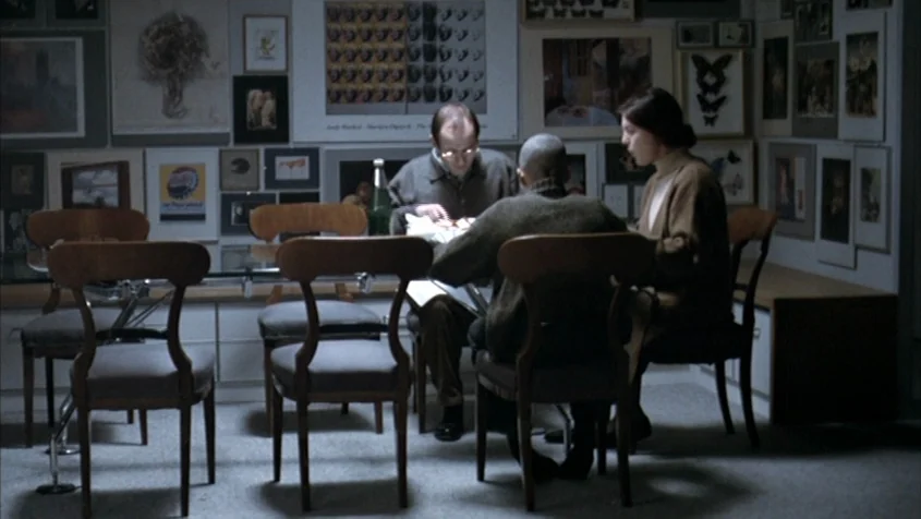 Benny’s Video (1992) movie still: medium — A dining area with framed art prints and butterfly displays covering the walls. Three individuals sit…