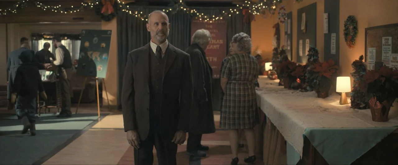 The Best Christmas Pageant Ever (2024) movie still: medium — A community hall decorated with holiday lights and poinsettias for a seasonal event. A…
