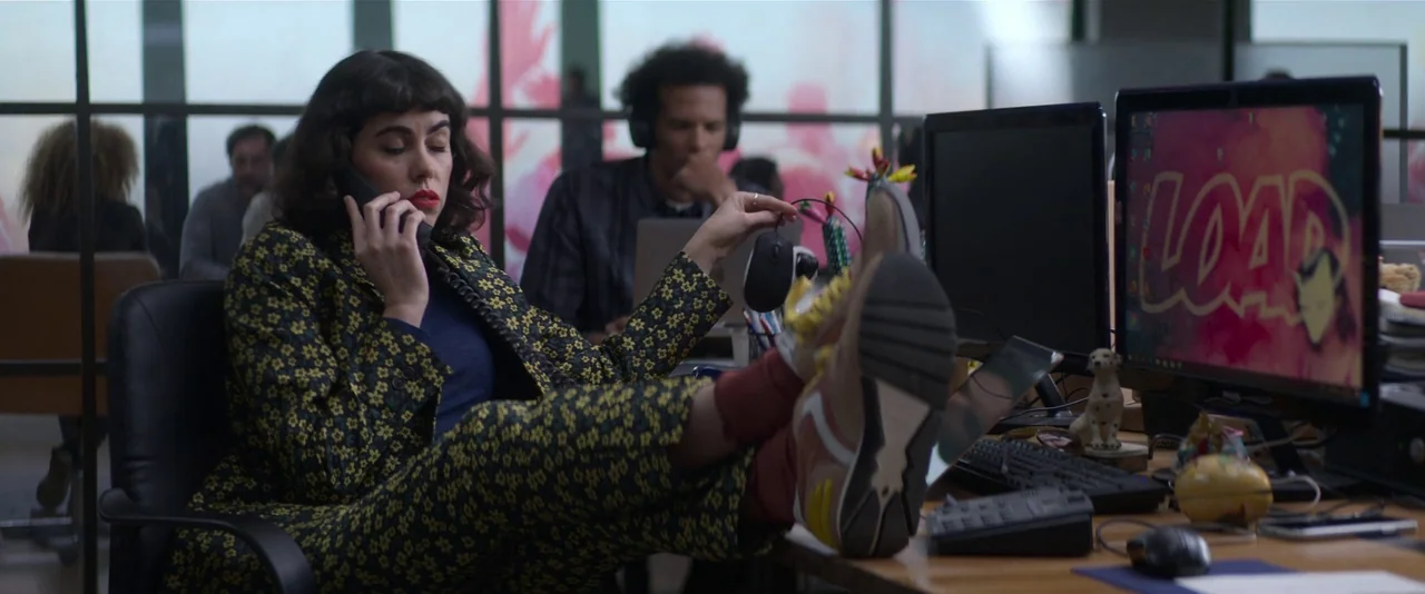 Crazy About Her (2021) movie still: medium — A modern workspace features glass partitions and multiple workstations with computers. A woman sits in…