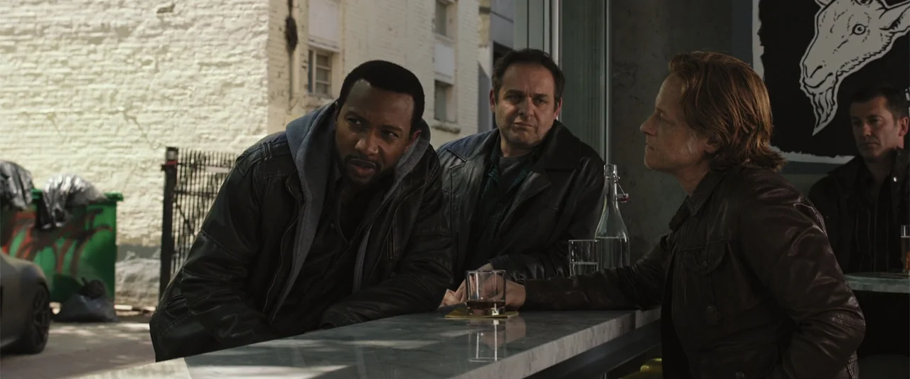 RoboCop (1987) movie still: medium — A modern bar counter sits adjacent to an open window overlooking a brick building. Three men stand together…