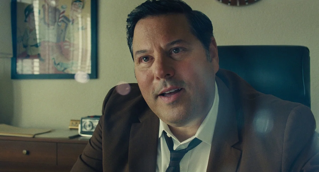The Fabelmans (2022) movie still: medium — A 1970s office interior features a framed print on a light-colored wall. A man sits in a chair wearing a…