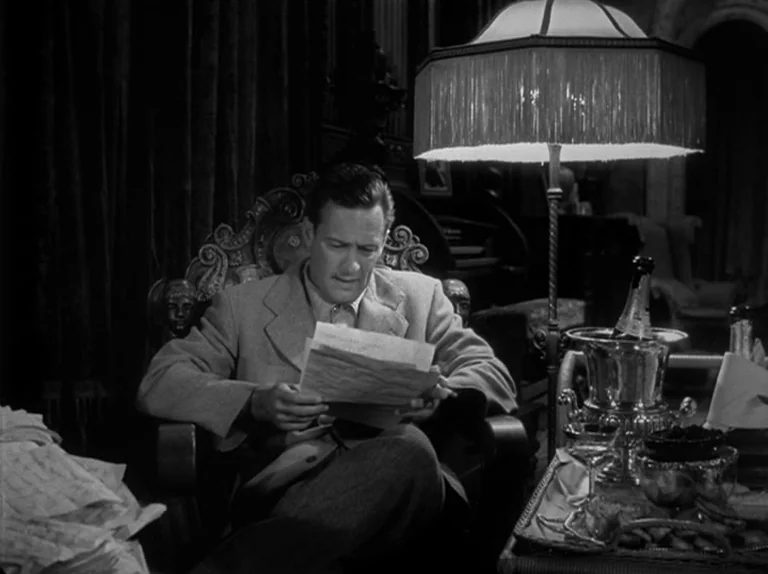 Sunset Boulevard (1950) movie still: medium — A dimly lit room with heavy drapes features a man reading in an armchair. A lamp with a fringe…