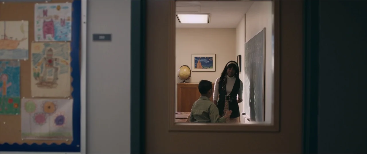 Woman of the Hour (2024) movie still: medium — A school classroom interior features a green chalkboard and a globe on a desk. A female teacher…