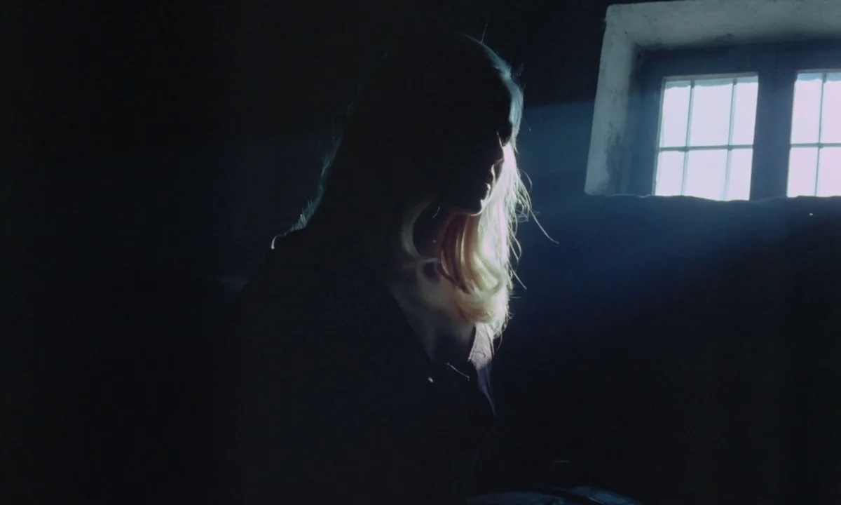 Vampyros Lesbos (1971) movie still: medium — A dimly lit room has a single small window emitting a beam of daylight. A woman sits in the darkness,…