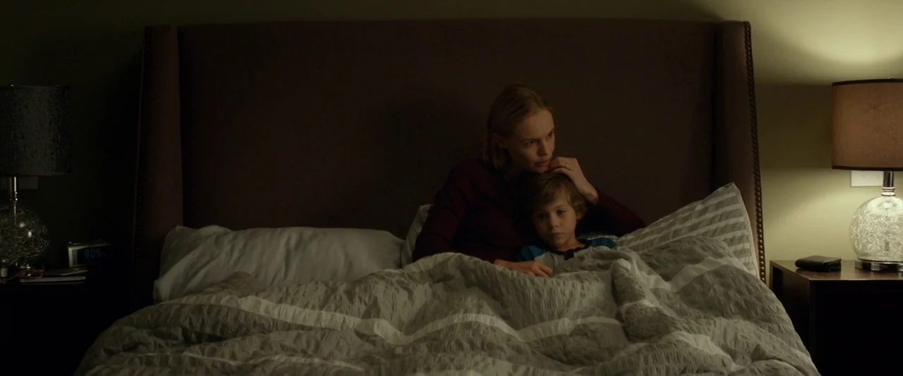 Before I Wake (2016) movie still: medium — A dimly lit bedroom features a large upholstered headboard and two nightstands. A woman is positioned…