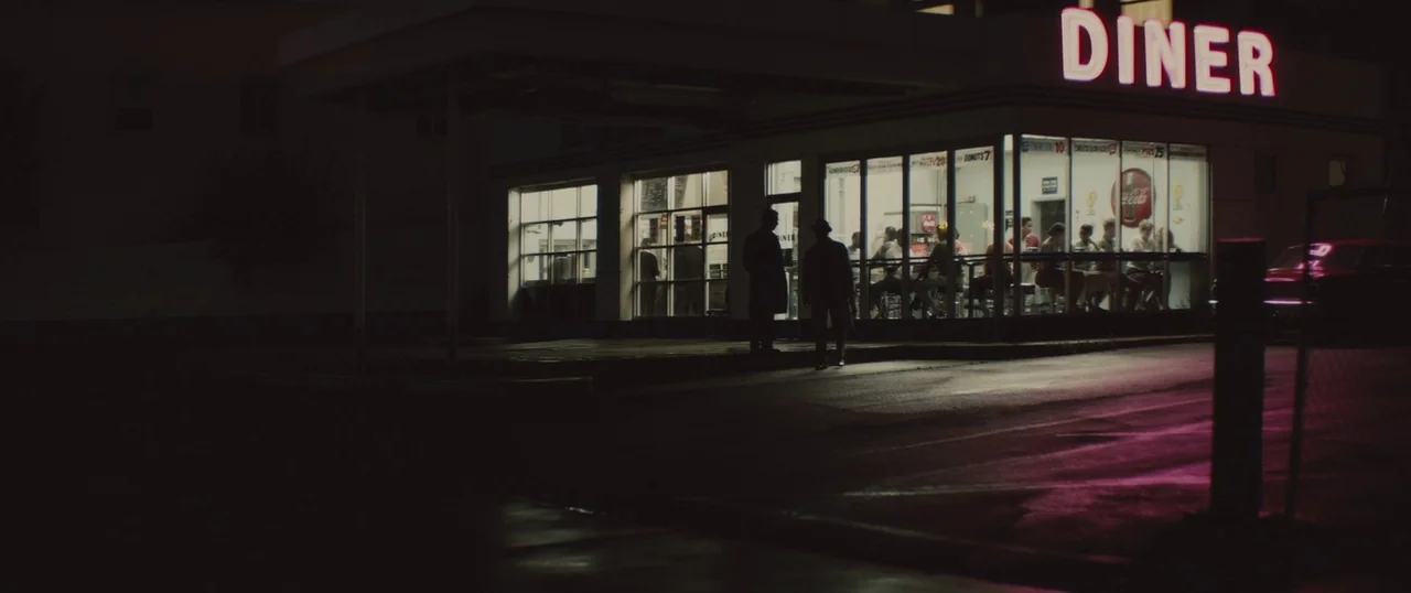 Selma (2014) movie still: wide — A 1950s diner at night features a glowing red neon sign and large glass windows. Two men in dark trench coats stand…