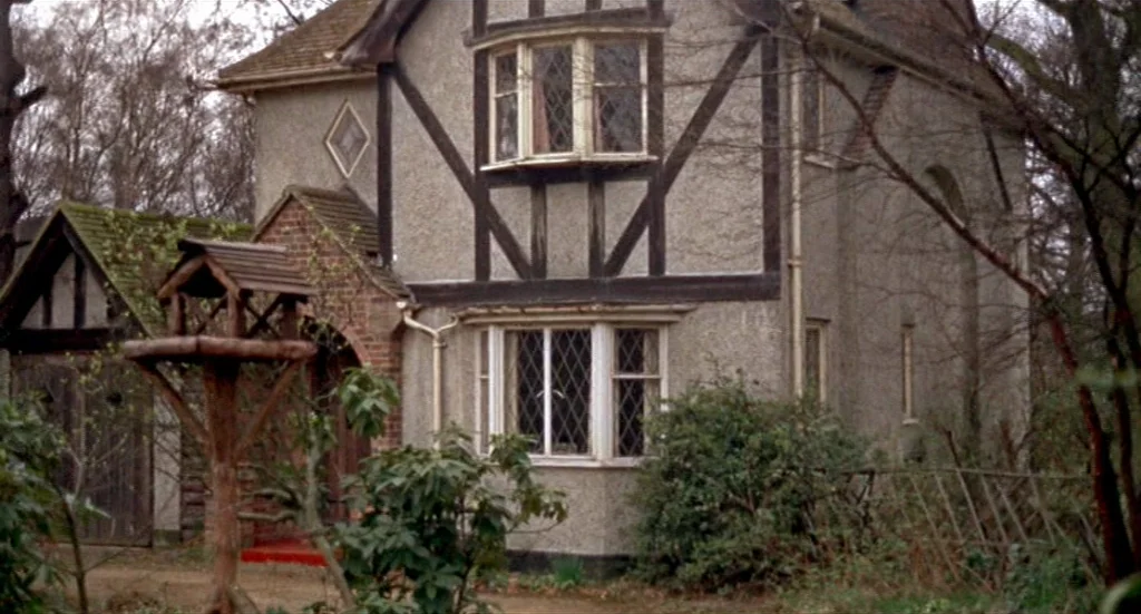 Fahrenheit 451 (1966) movie still: establishing — A two-story Tudor-style cottage with stucco walls and timber framing sits amidst bare trees. A…