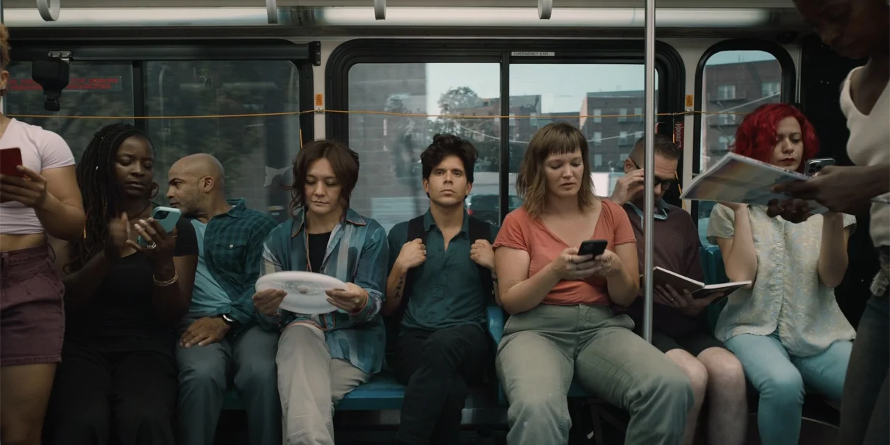 Música (2024) movie still: medium — A group of diverse passengers sit in a row on blue seats inside a bus. They occupy themselves with smartphones…