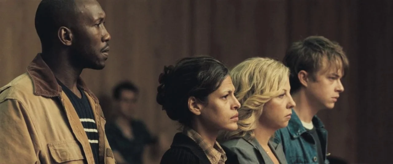 The Place Beyond The Pines (2012) movie still: medium — A row of four people sits against wood-paneled walls in a courtroom environment. The…